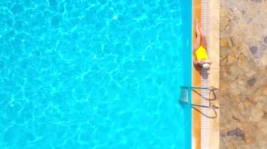 Sarı mayolu ve havuzun kenarında duran şapkalı bir kadının yukarıdan görünüşü. Yaz yaşam tarzı, dinlenme ve rahatlama kavramı