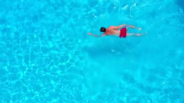 Havuzda yüzen kırmızı şortlu bir adamın hava görüntüsü. Yaz yaşam tarzı