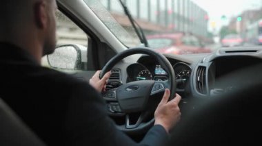 Adam yağmur yağarken şehirde yol boyunca araba sürüyor. Şehir trafiği, arabalar, trafik ışıkları. Sürücülerin omzunun arkasından bak.