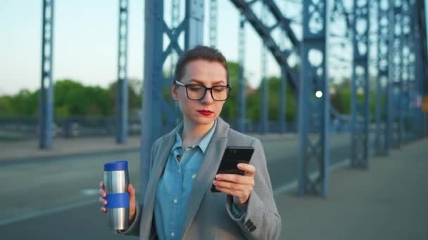 身穿外套的白人女商人 一大早在城市里走来走去 喝咖啡 用智能手机 工作日 忙碌生活概念 — 图库视频影像