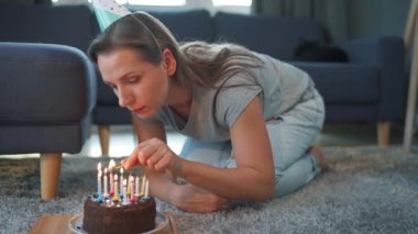 Doğum günü pastasında mum yakan bir kadın, evde yalnız başına doğum gününü kutluyor.