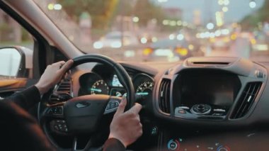 Adam yağmurdan sonra akşam şehrinin sokaklarında araba sürüyor. Şehir ışıkları, arabalar, trafik ışıkları, arabanın camındaki binalar. Arabanın arka koltuğundan bak..