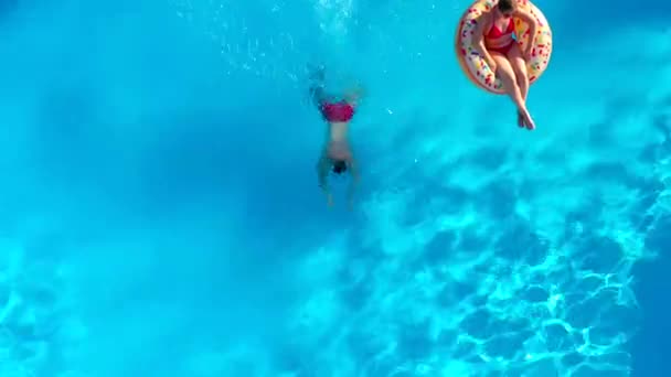 トップダウンビューの男はプールに飛び込み 女の子はドーナツプールのフロートに横たわっている間に泳ぐ — ストック動画