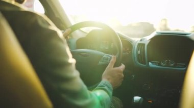 Adam yol boyunca araba sürüyor, batan güneş ön camda parlıyor. Sürücülerin omzunun arkasından bak.