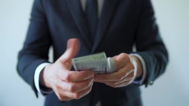 Resmi olarak giyinmiş bir adam Amerikan dolarlarını sayıyor, yakın plan. Yatırım, başarı, finansal beklentiler veya kariyer ilerlemesi kavramı