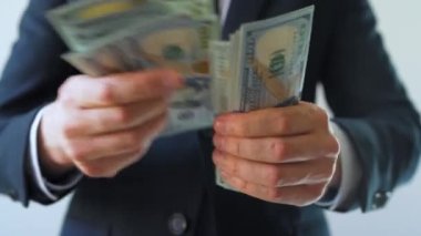Resmi olarak giyinmiş bir adam Amerikan dolarlarını sayıyor, yakın plan. Yatırım, başarı, finansal beklentiler veya kariyer ilerlemesi kavramı