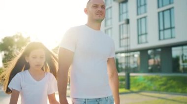 Baba ve kızı gün batımında kendi bölgelerinde dolaşırlar. Çocuk babasının elini tutuyor. Yavaş çekim