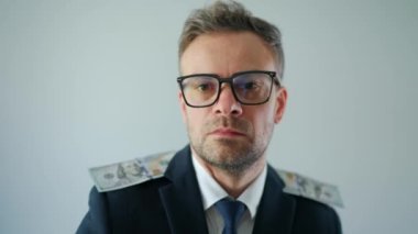 Formally dressed man with glasses made his shoulder straps out of US dollar bills and grimaces at the camera. Funny video