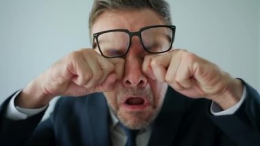 Funny portrait of a confused businessman - first he rubs his eyes under his glasses, and then looks into the camera