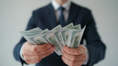 Resmi olarak giyinmiş bir adam Amerikan dolarlarını sayıyor, yakın plan. Yatırım, başarı, finansal beklentiler veya kariyer ilerlemesi kavramı