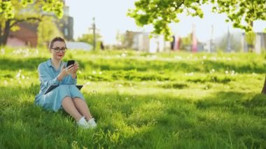 Gün batımında açık havada işi bittikten sonra parkta otururken akıllı telefon kullanan bir kadın. Dışarıda çalışan serbest çalışan biri.