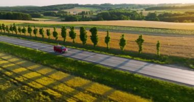 Aerial view of the road and car driving along it at sunset. On the sides of the road are fields during harvest.