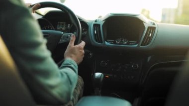 Adam yol boyunca araba sürüyor, batan güneş ön camda parlıyor. Sürücülerin omzunun arkasından bak.