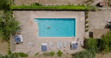 Top down view of a woman in red swimsuit swimming in the pool. Camera descends over the pool. Summer lifestyle