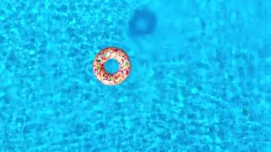 Top down view as a man dives into the pool and swims, inflatable donut is there