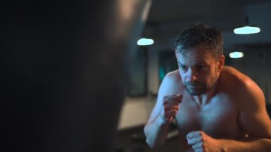 Alone male boxer is working out blows on a punching bag in a gym in evening. Slow motion