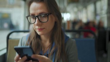 Toplu taşıma. Tramvayda gözlüklü bir kadın akıllı telefon sohbeti yapıyor ve arkadaşlarıyla mesajlaşıyor. Şehir, şehir, ulaşım.