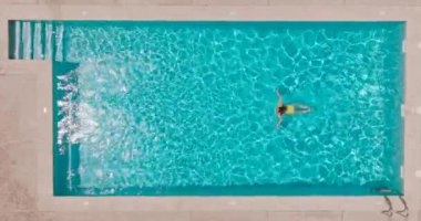 Top down view of a woman in yellow swimsuit swimming in the pool. Summer lifestyle