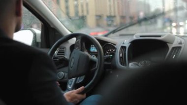 Adam yağmur yağarken şehirde yol boyunca araba sürüyor. Şehir trafiği, arabalar, trafik ışıkları. Sürücülerin omzunun arkasından bak.