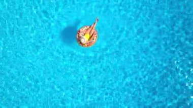 Top down view of a woman in yellow swimsuit lying on a donut in the pool. Concept of summer lifestyle, rest and relaxation