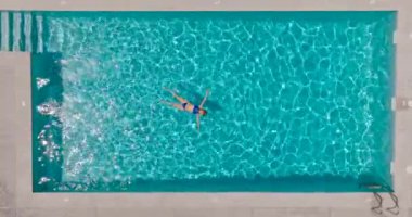 Top down view of a woman in a blue swimsuit lying on her back in the pool. Relaxing concept, summer lifestyle