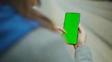 Caddedeki kadın dikey modda yeşil ekran akıllı telefon kullanıyor. Kız internette geziniyor, içeriği, videoları, blogları izliyor.