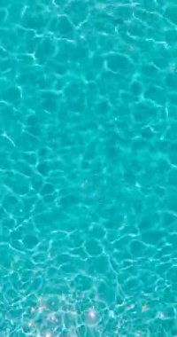 Vertical video. Surface of pure blue water in the swimming pool with light reflections. Aerial footage