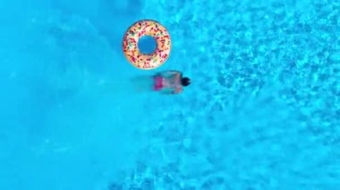 Top down view as a man dives into the pool and swims, inflatable donut is there