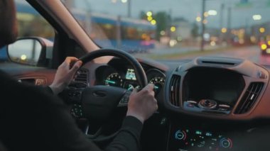 Akşam şehrinin sokaklarında araba süren bir adam. Şehir ışıkları, arabalar, trafik ışıkları, arabanın camındaki binalar. Arabanın arka koltuğundan bak..