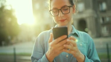 Woman using smartphone while standing outdoors at sunset. Communication, work day, busy life concept.