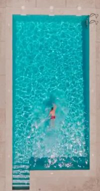 Vertical video. Aerial view of a man in red shorts swimming in the pool. Summer lifestyle