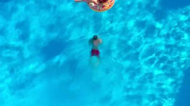 Top down view of a couple having fun in the pool, the man dives and the woman lies on an inflatable donut