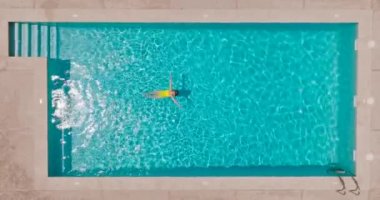 Top down view of a woman in an yellow swimsuit lying on her back in the pool. Relaxing concept, summer lifestyle