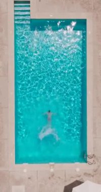 Vertical video. Top down view as a man dives into the pool and swims. Slow motion