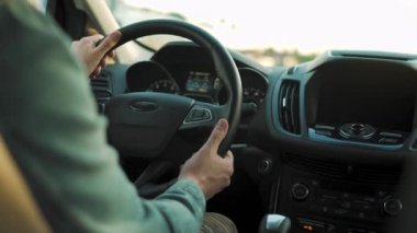 Adam yol boyunca araba sürüyor, batan güneş ön camda parlıyor. Sürücülerin omzunun arkasından bak.