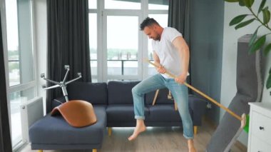 Adam evi temizliyor ve süpürgeyle dans ediyor. Yavaş çekim. 