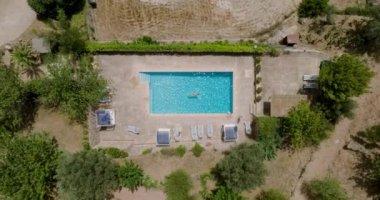 Top down view of a woman in red swimsuit lying on her back in the pool. Camera descends over the pool. Relaxing concept, summer lifestyle