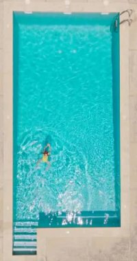 Vertical video. Top down view of a woman in yellow swimsuit swimming in the pool. Summer lifestyle