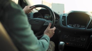 Adam yol boyunca araba sürüyor, batan güneş ön camda parlıyor. Sürücülerin omzunun arkasından bak.