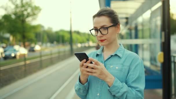 Woman Stands Public Transport Stop Using Smartphone Waiting Tram City — Vídeo de Stock