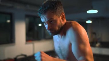 Alone male boxer is working out blows on a punching bag in a gym in evening.