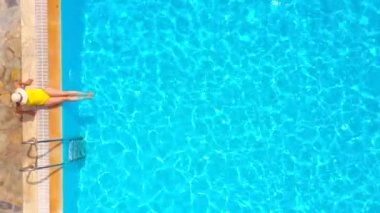 Sarı mayolu ve şapkalı bir kadın havuzun kenarında oturuyordu. Yaz yaşam tarzı, dinlenme ve rahatlama kavramı