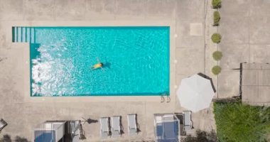 Top down view of a woman in an yellow swimsuit lying on her back in the pool. Relaxing concept, summer lifestyle