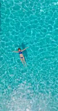 Vertical video. Top down view of a woman in a blue swimsuit lying on her back in the pool. Relaxing concept, summer lifestyle