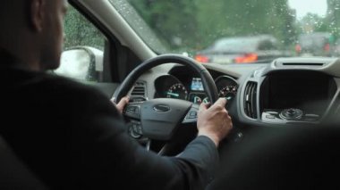 Adam yağmur yağarken şehirde yol boyunca araba sürüyor. Şehir trafiği, arabalar, trafik ışıkları. Sürücülerin omzunun arkasından bak.