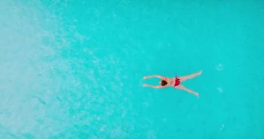 Top down view of a woman in red swimsuit swimming in the pool. Summer lifestyle