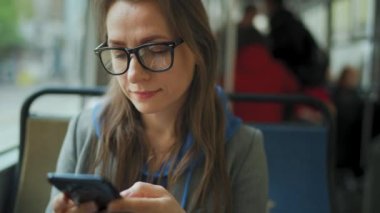 Toplu taşıma. Tramvayda gözlüklü bir kadın akıllı telefon sohbeti yapıyor ve arkadaşlarıyla mesajlaşıyor. Şehir, şehir, ulaşım.