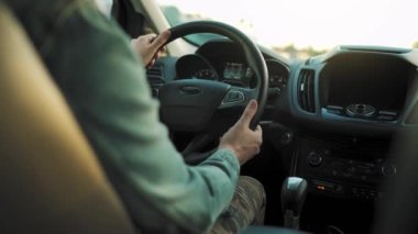 Adam yol boyunca araba sürüyor, batan güneş ön camda parlıyor. Sürücülerin omzunun arkasından bak.