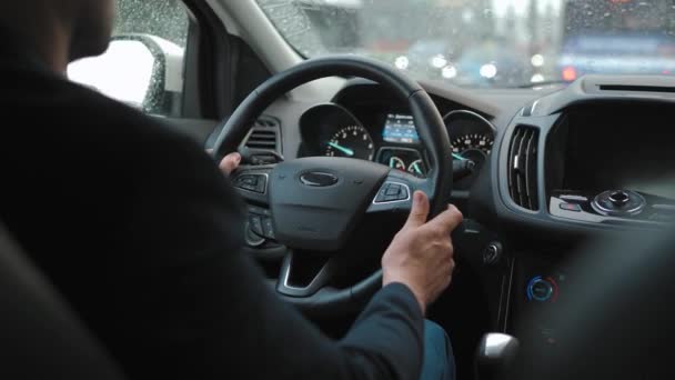 男は雨の中 市内の道路に沿って車を運転する 市内の交通 信号機の周り ドライバーの肩の後ろからの眺め — ストック動画