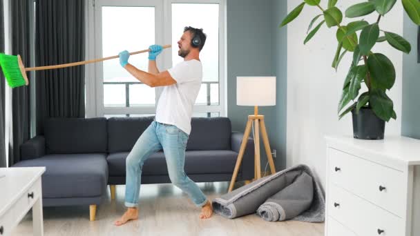 头戴耳机的白人男人打扫房子 一边跳舞一边用扫帚唱歌 慢动作 — 图库视频影像